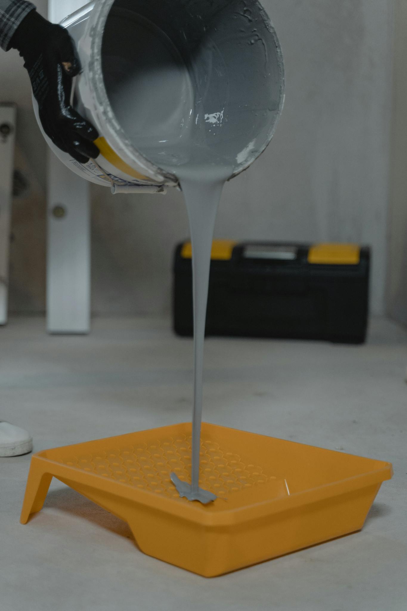 Gray paint pouring into a yellow tray, ideal for room renovation projects.
